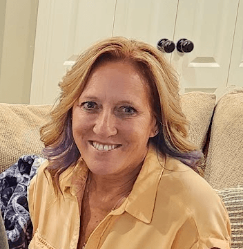 Smiling woman with blonde hair and purple tips wearing a yellow collared shirt.