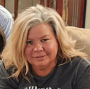 A woman with wavy blonde hair and a slight smile wearing a casual gray t-shirt.