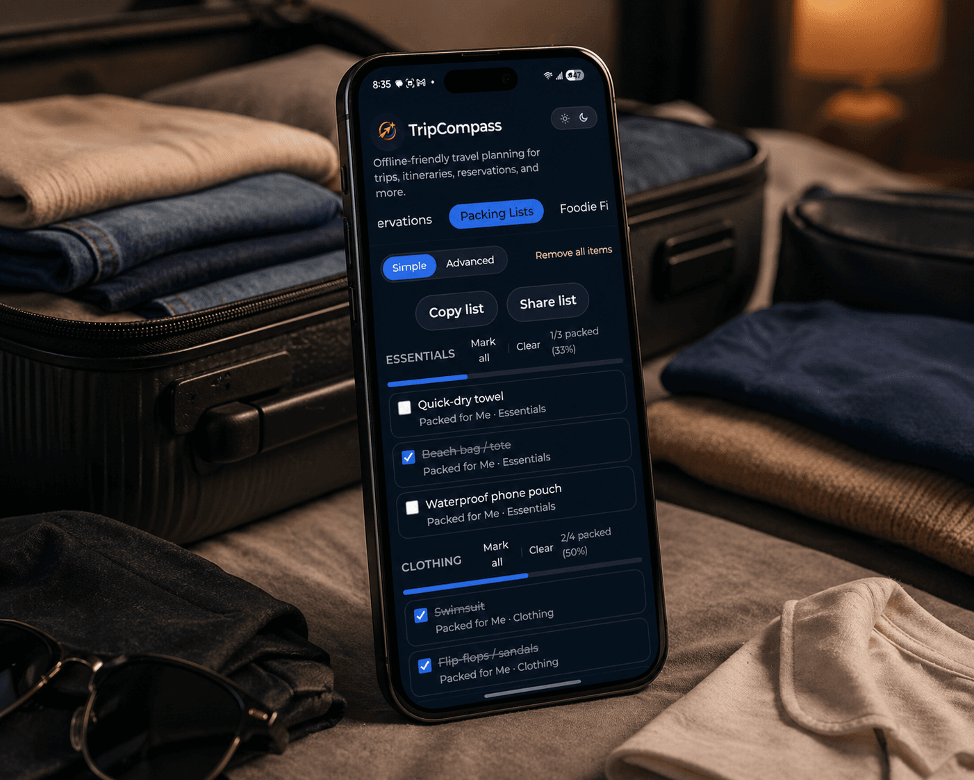 Smartphone displaying a travel packing list app among folded clothes and an open suitcase.